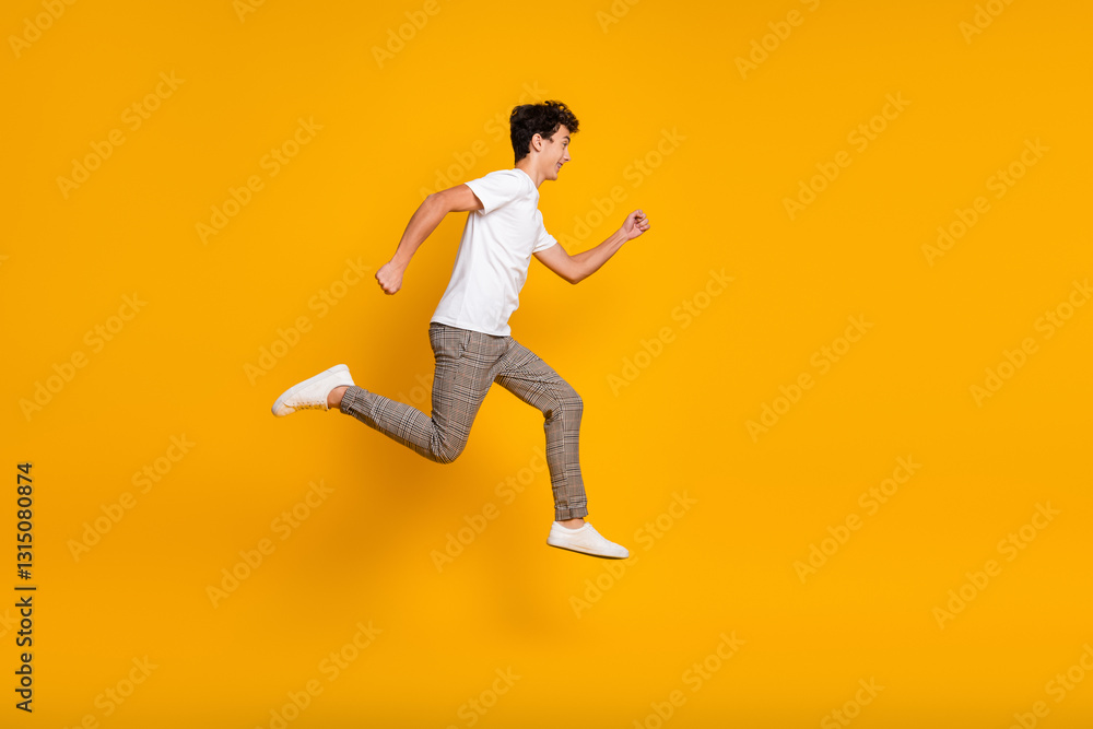 Fototapeta premium Young man in white t-shirt jumping with joy on vibrant yellow background, expressing happiness, energy, and a casual trendy style