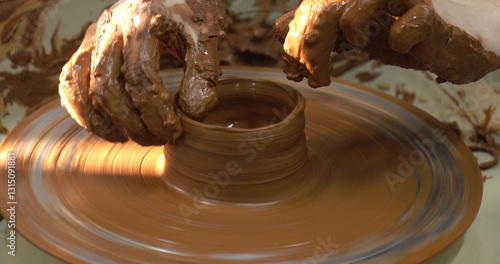 Obraz na płótnie The potter's wheel. A close-up of the hands of a craftsman skillfully working with clay on a potter's wheel, giving it the shape of a clay product w salonie