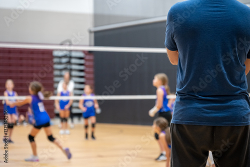Selective focus behind a coach at a youth volleyball match, blurred game. 