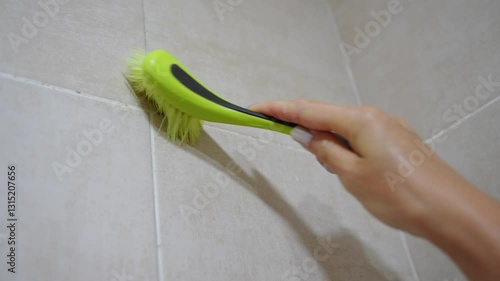 Cleaning black mold on grout between bathroom tiles with squeegee in damp, poorly ventilated bathroom, close-up. Dampness problem in bathrooms, getting rid of mold indoors