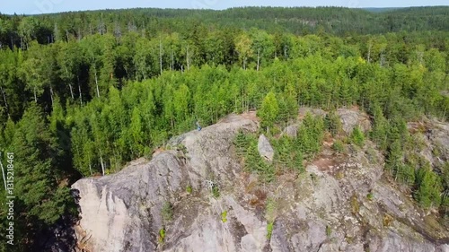 Man standing on high rock, mountain surrounded by forest and lake. Concept travel, tourism, achievement, victory, overcoming. Aerial shot around.