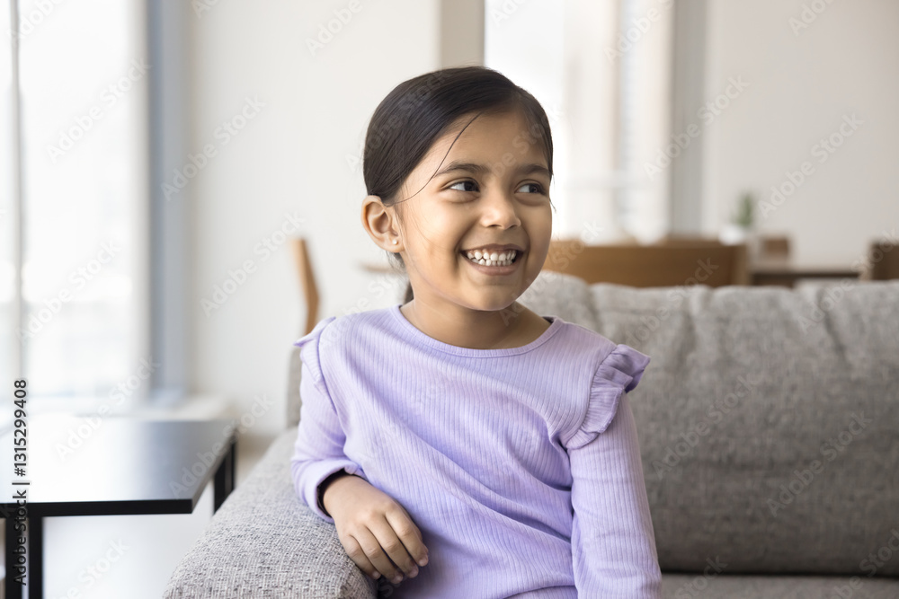 Cute Indian girl looking into distance seated on couch at home, wearing lavender long-sleeve top, sitting comfortably on sofa in cozy living room, smiling, exuding innocence, happiness, and curiosity Cute Indian girl looking into distance seated on couch at home, wearing lavender long-sleeve top, sitting comfortably on sofa in cozy living room, smiling, exuding innocence, happiness, and curiosity