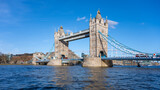 Tower Bridge stands majestically against a clear blue sky in London. The sunlight highlights its unique architecture and the flowing river beneath showcases a perfect day for exploration.