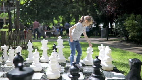 Adorable preschooler girl playing chess with big chess pieces outdoors on a sunny summer day.