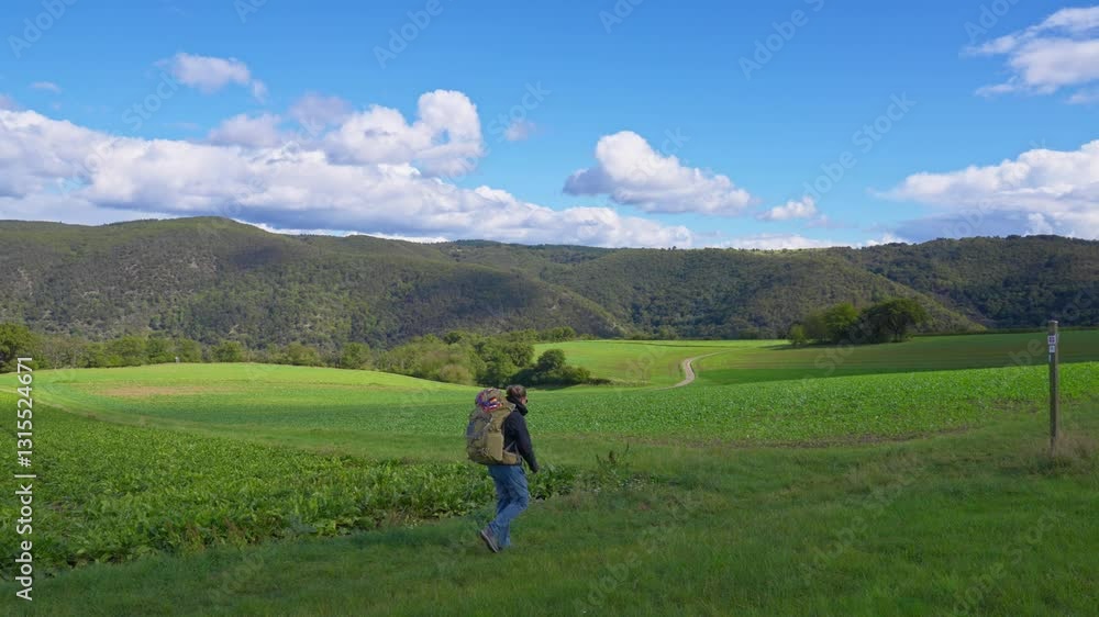 One person walking with large backpack on a green meadow while surrounded by panoramic nature views during a sunny summer day, Rhine Valley, Germany One person walking with large backpack on a green meadow while surrounded by panoramic nature views during a sunny summer day, Rhine Valley, Germany