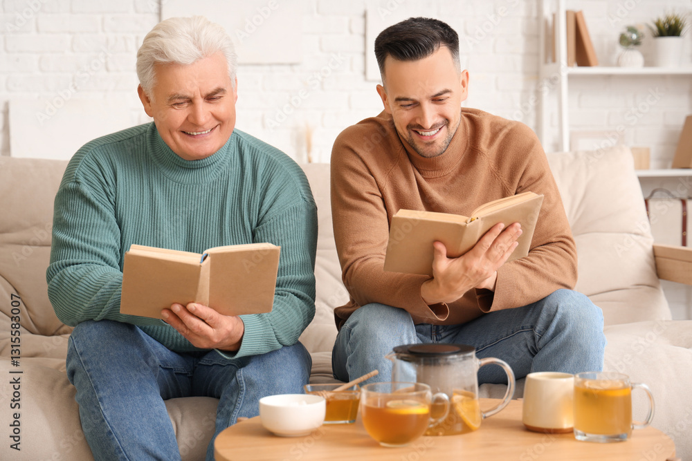 Young man with his father drinking lemon tea and reading books at home Young man with his father drinking lemon tea and reading books at home