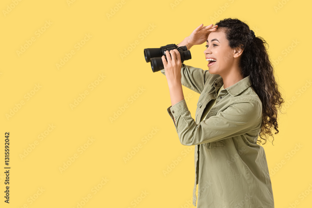 Obraz premium Young African-American woman with binoculars on yellow background