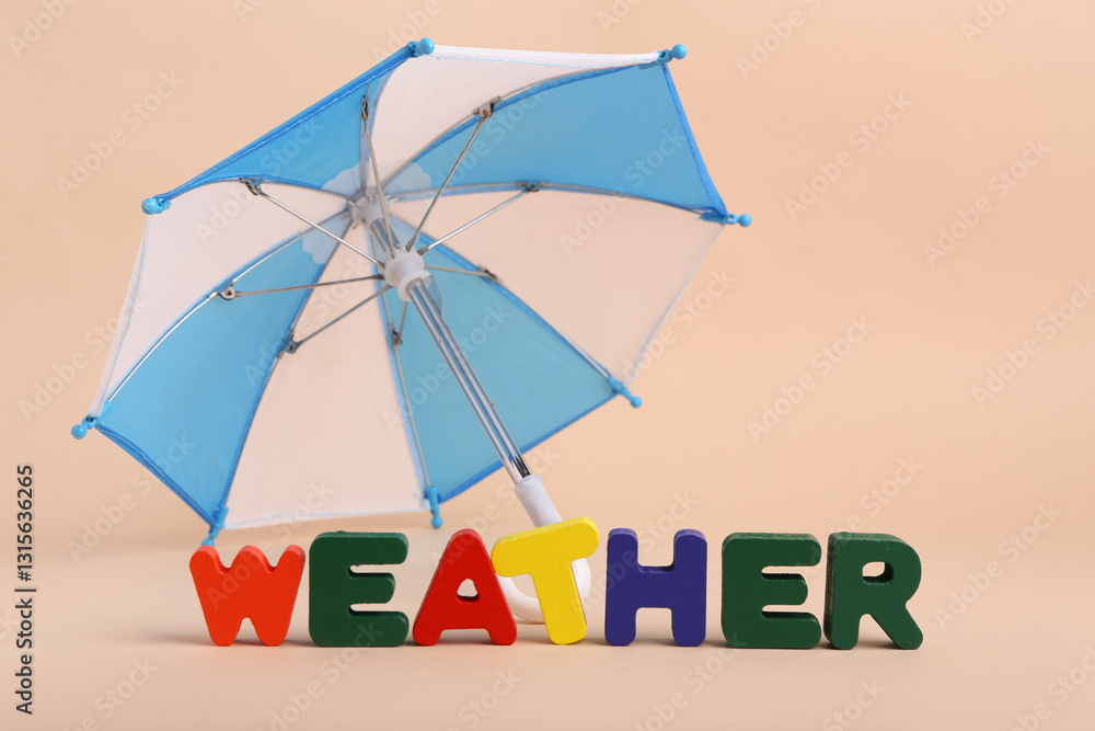 Fototapeta premium Mini umbrella and word WEATHER made of colorful letters on beige background