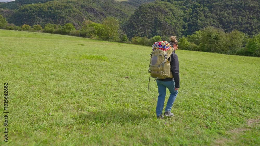 Following hiking backpacker walking down a hilly green grass meadow landscape in slow motion Following hiking backpacker walking down a hilly green grass meadow landscape in slow motion