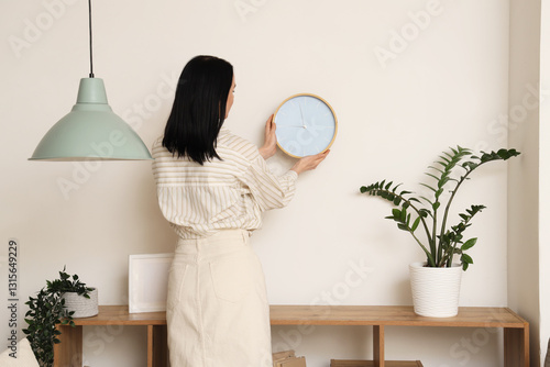 Young woman hanging clock n...