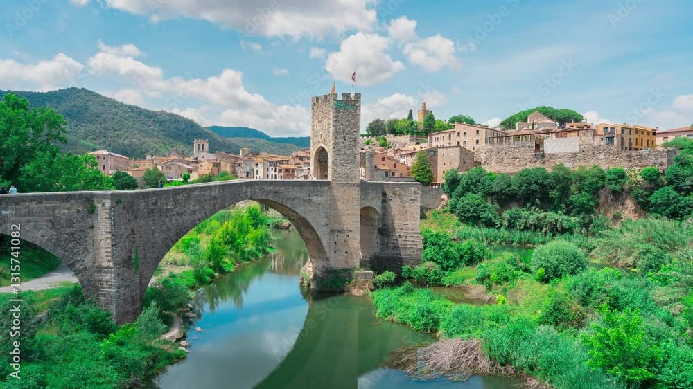 Bridge of a medieval city over a river with vegetation and mountains in the background, a sunny day with blue sky and clouds moving due to accelerated time. Bridge of a medieval city over a river with vegetation and mountains in the background, a sunny day with blue sky and clouds moving due to accelerated time.
