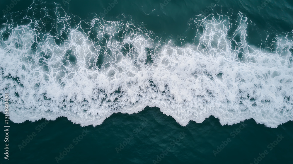 Aerial view of ocean waves crashing onto shore, creating white foam patterns against deep blue water. natural movement of sea is captured in dynamic and textured composition