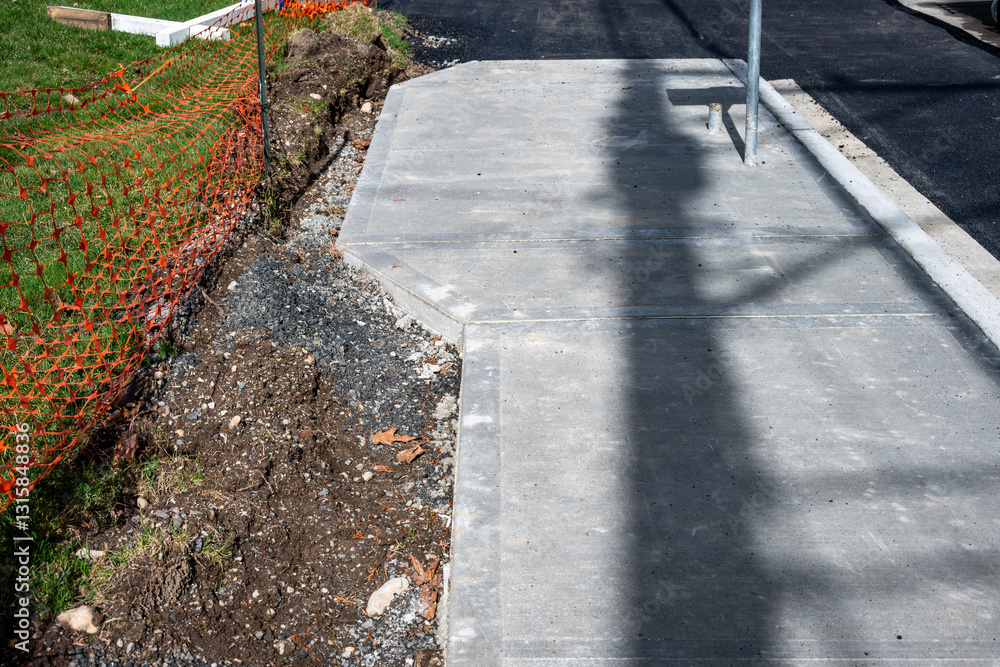 Obraz premium Public works road paving and sidewalk installation project, fresh asphalt and new cement sidewalk with storm drain at curb 
