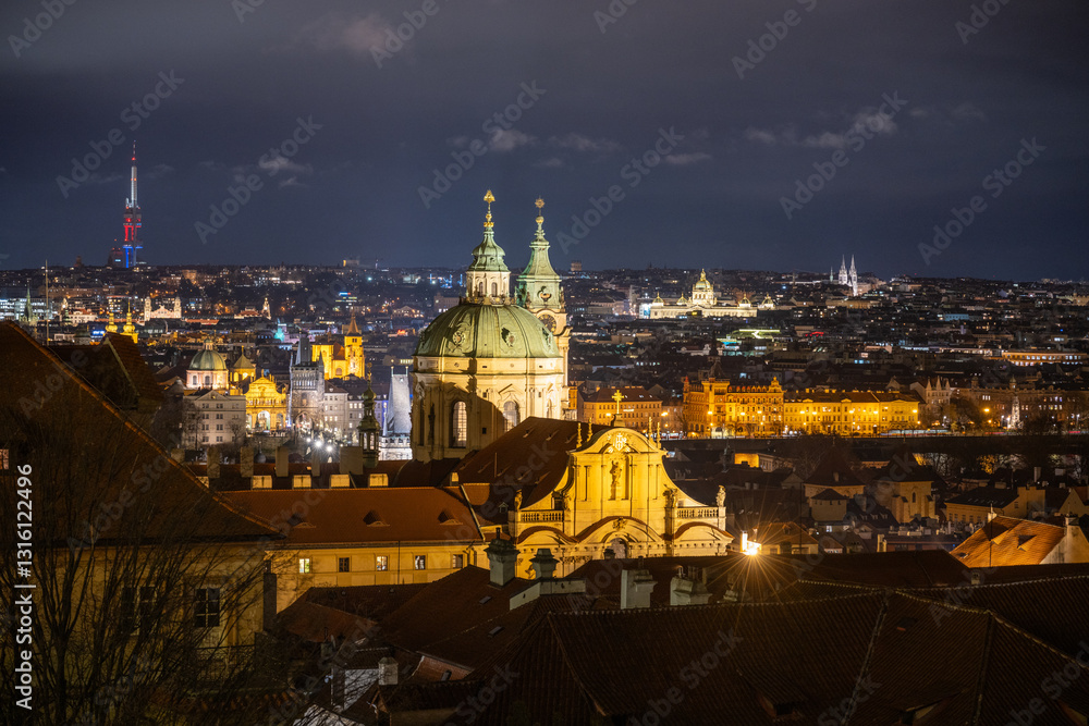 Obraz premium Illuminated against the night, the Church of St Nicholas stands prominently in Lesser Town, showcasing its Baroque design. The vibrant city lights enhance the view of Prague.