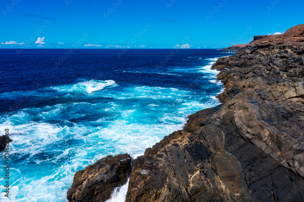 Obraz premium Stunning Coastal Landscape of Fuerteventura with Turquoise Waves Breaking Against Dark Volcanic Cliffs. Dramatic Ocean Scenery from Canary Islands