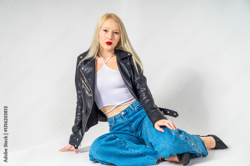 Pretty blonde girl sitting on white background. Model is wearing black leaher jacket and blue jeans. Copy space Pretty blonde girl sitting on white background. Model is wearing black leaher jacket and blue jeans. Copy space
