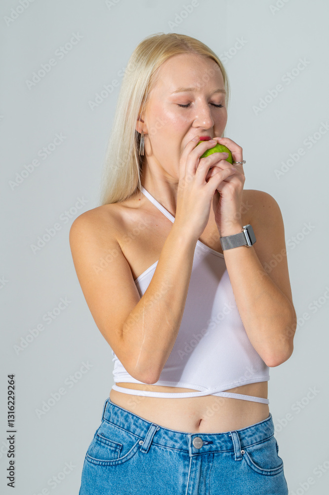 Attractive young blonde holding an apple. She is wearing a white top and blue jeans on a white background. Copy space Attractive young blonde holding an apple. She is wearing a white top and blue jeans on a white background. Copy space