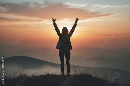 A woman standing alone on a hilltop, raising both hands in joy and triumph.