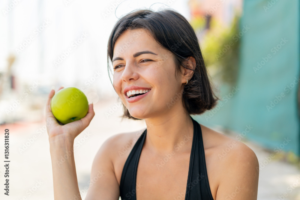 Young pretty Bulgarian woman at outdoors holding an apple with happy expression Young pretty Bulgarian woman at outdoors holding an apple with happy expression