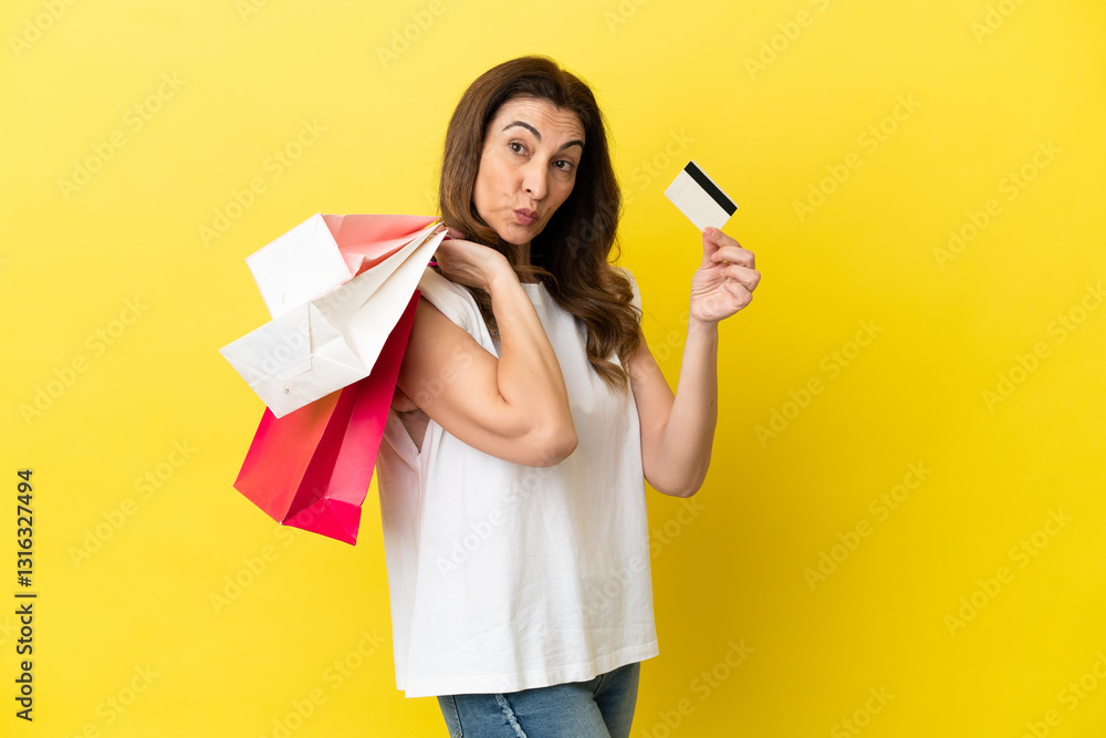 Middle aged caucasian woman isolated on yellow background holding shopping bags and a credit card Middle aged caucasian woman isolated on yellow background holding shopping bags and a credit card