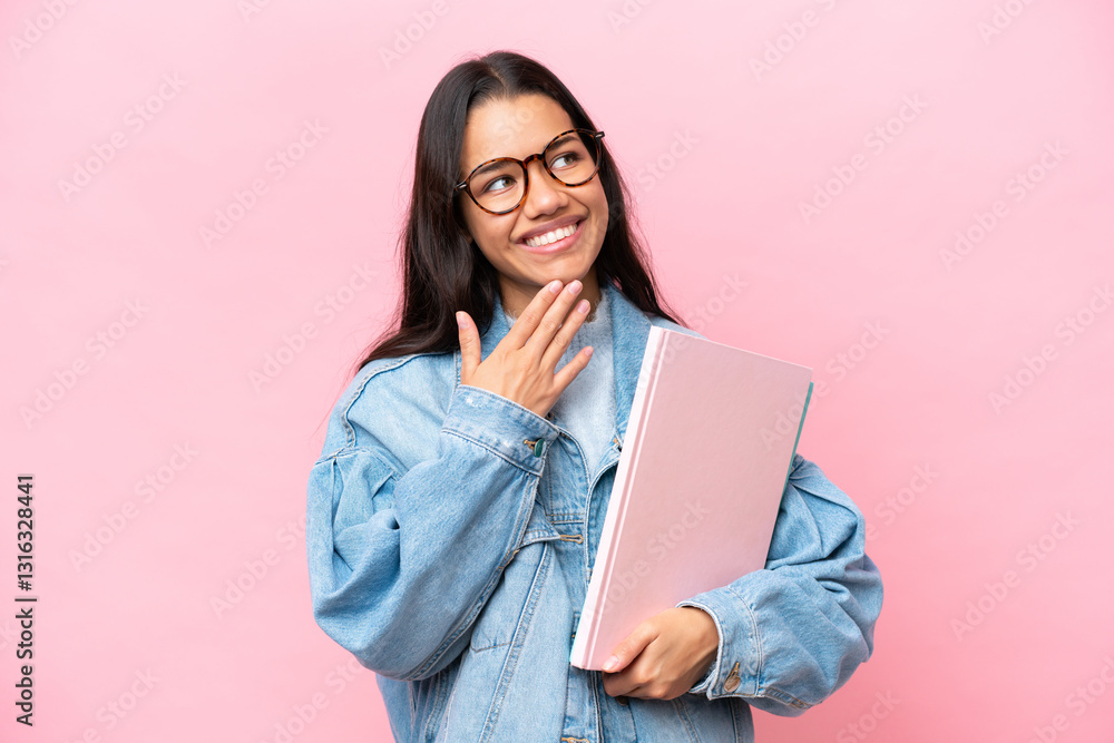 Fototapeta premium Young student Colombian woman isolated on pink background looking up while smiling