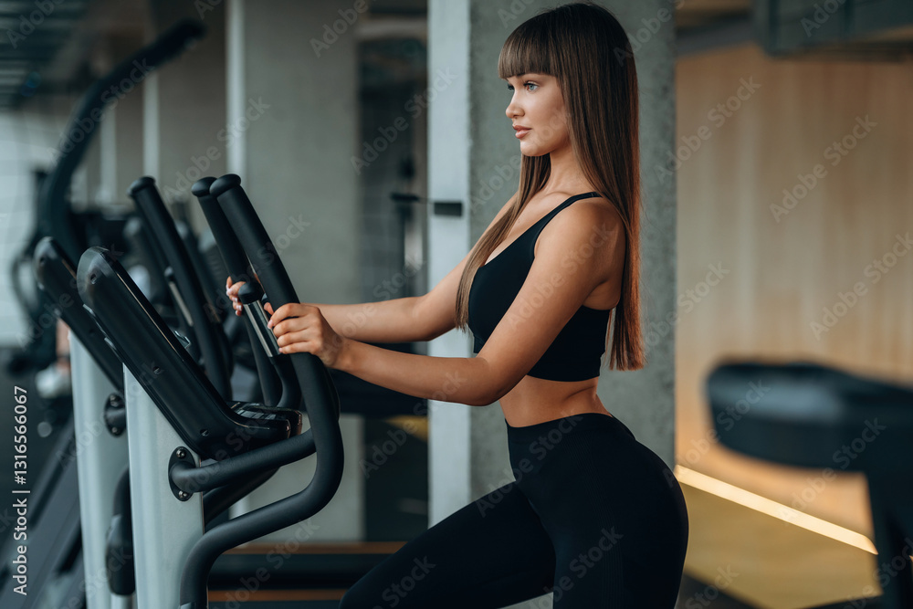 View from the side, on the bicycle. Young woman is in the gym View from the side, on the bicycle. Young woman is in the gym