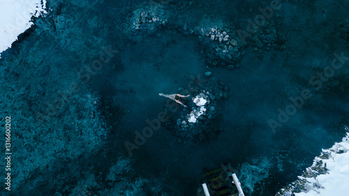 Aerial view of a lone woman relaxing in a stunning thermal spring surrounded by snowy landscapes in Northern Buryatia. Winter serenity and natural beauty.