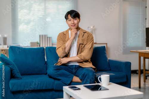 Free Download Pensive male resting on home sofa, leaning chin on hand, expressing deep contemplation and calm introspection - GFXLoad