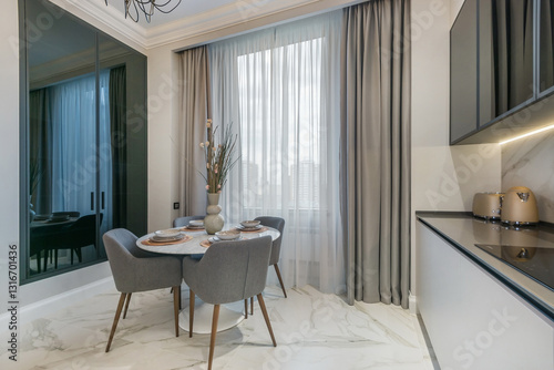 Elegant table setting in the interior of a modern kitchen. Built-in wardrobe with dark glass doors, window with beautiful drapery.