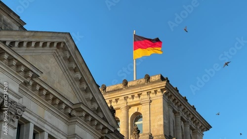 The German flag waves atop the historic reichstag building with classical architectural elements against a clear blue sky