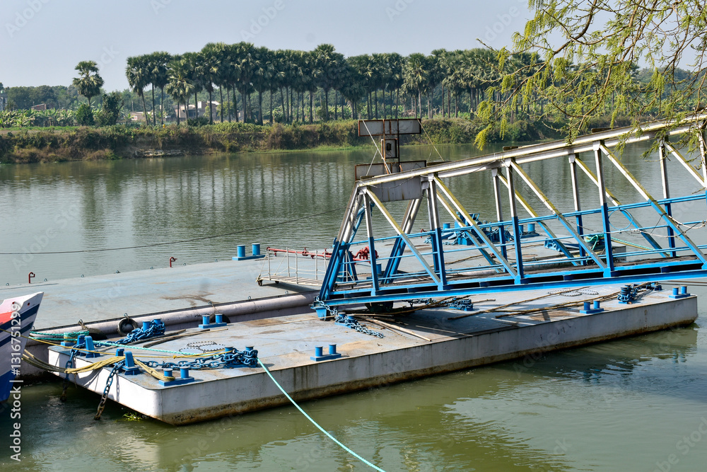 Fototapeta premium This image features a metallic blue floating pontoon bridge or ferry dock on a calm Ganges River