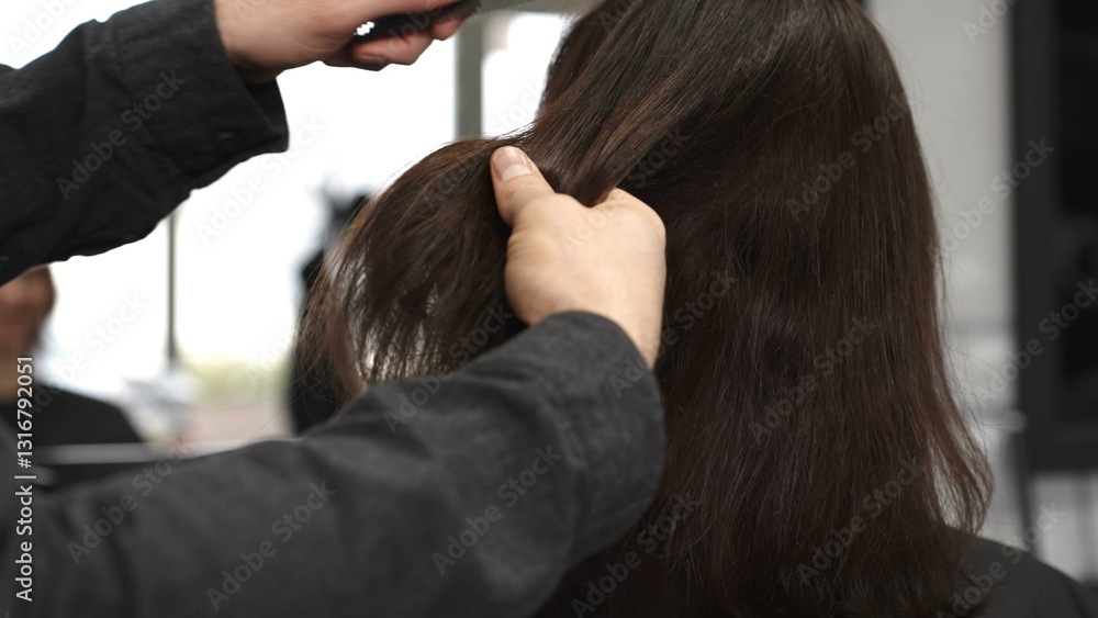 Fototapeta premium Professional hairdresser carefully combing sleek brown hair, working precisely within bright modern salon setting, preparing for transformative styling session