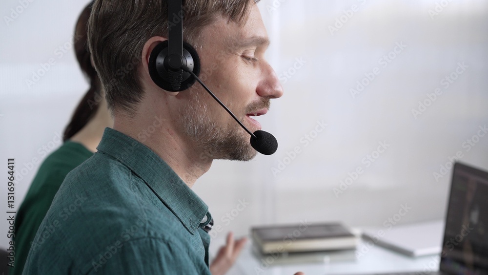 Focused male call center operator in green casual shirt is assisting clients online, providing customer support and answering inquiries. Call center concept