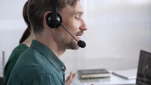 Obraz na płótnie Focused male call center operator in green casual shirt is assisting clients online, providing customer support and answering inquiries. Call center concept w salonie
