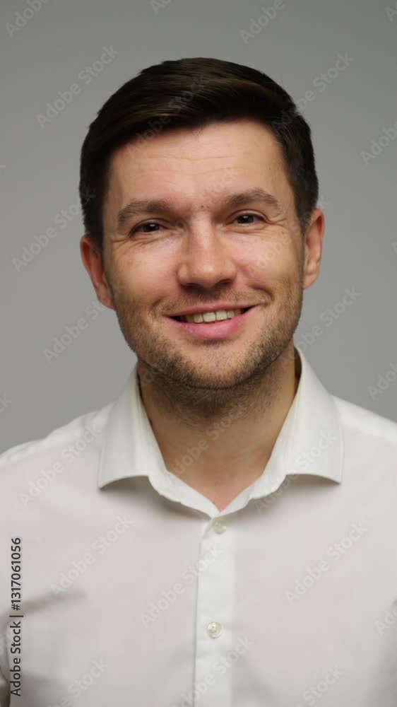 Smiling young man in white shirt standing confidently against a light background Smiling young man in white shirt standing confidently against a light background