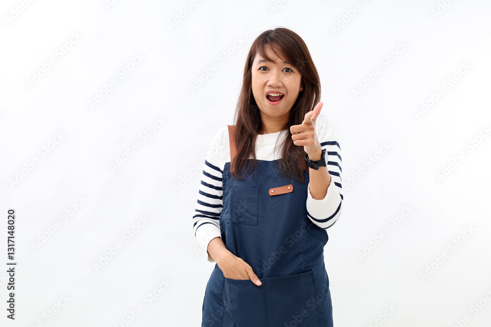 Naklejka premium Beautiful asian barista in blue apron welcome guests to coffee shop, pointing finger gun, standing against white background