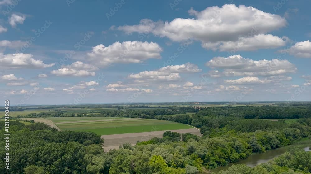 A serene view of a river surrounded by lush green forests and distant hills under a bright blue sky with fluffy clouds, capturing the peacefulness of nature on a sunny day. A serene view of a river surrounded by lush green forests and distant hills under a bright blue sky with fluffy clouds, capturing the peacefulness of nature on a sunny day.