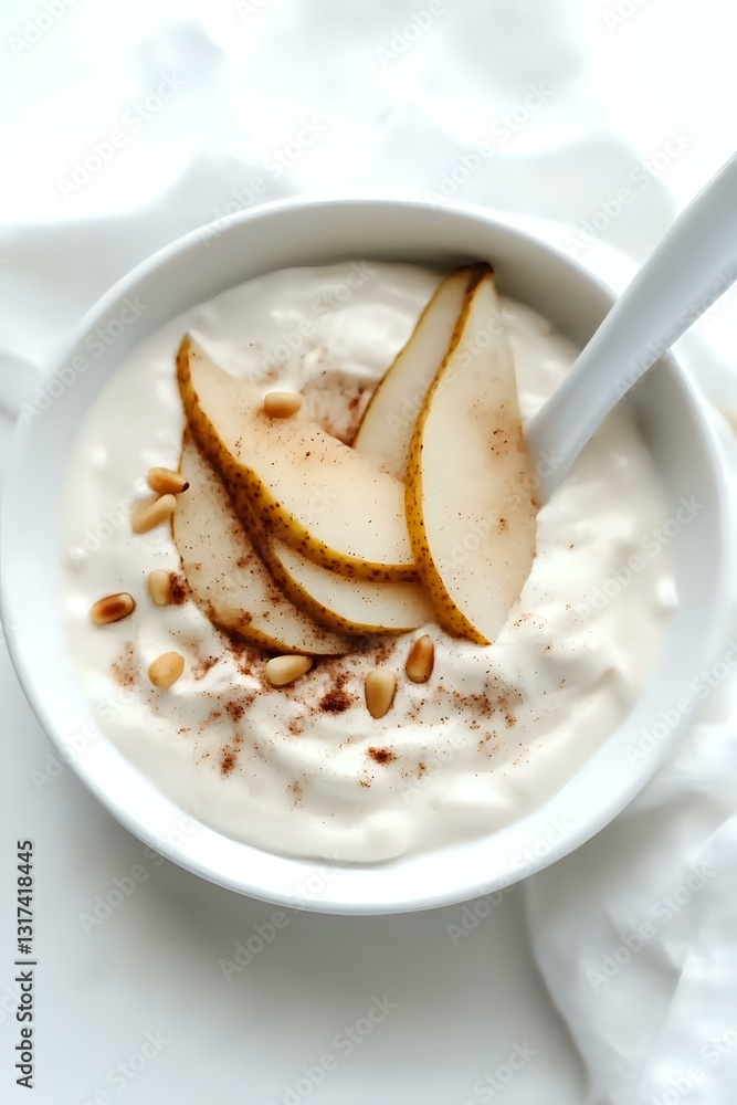 Fresh sliced pears with pine nuts and cinnamon served over creamy white yogurt in ceramic bowl, high-key food photography on light background. Fresh sliced pears with pine nuts and cinnamon served over creamy white yogurt in ceramic bowl, high-key food photography on light background.
