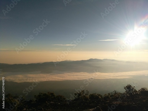 The majestic charm of a mountain towering above a sea of clouds, bathed in golden sunlight that radiates magical beauty.
