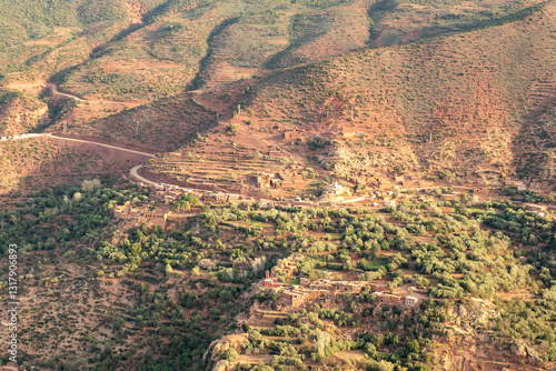 A panoramic view of the majestic Atlas Mountains in Morocco, contrasting against a clear blue sky. Lush green valleys wind through the rugged terrain,.