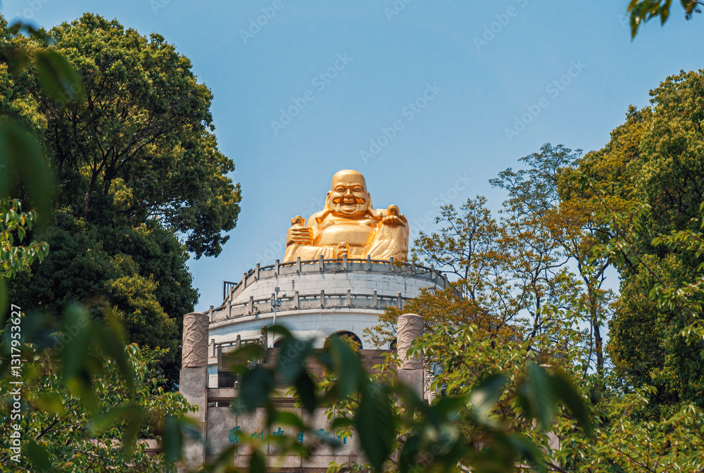 A magnificent golden Buddha statue sits atop a temple, surrounded by vibrant trees and foliage under a bright blue sky. A magnificent golden Buddha statue sits atop a temple, surrounded by vibrant trees and foliage under a bright blue sky.