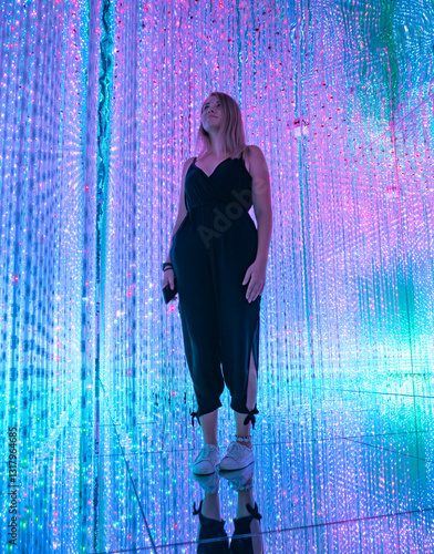 Young woman stands surrounded by colorful lights in an immersive art installation.