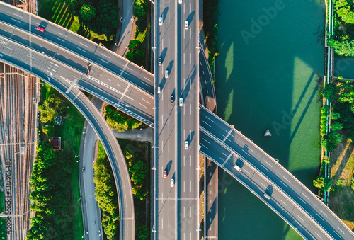 Aerial view of multiple highways intersect above a calm river, surrounded by vibrant greenery.