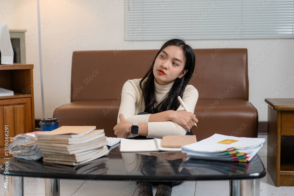 Young professional woman looking away and thinking about work at home office with documents and books on table Young professional woman looking away and thinking about work at home office with documents and books on table