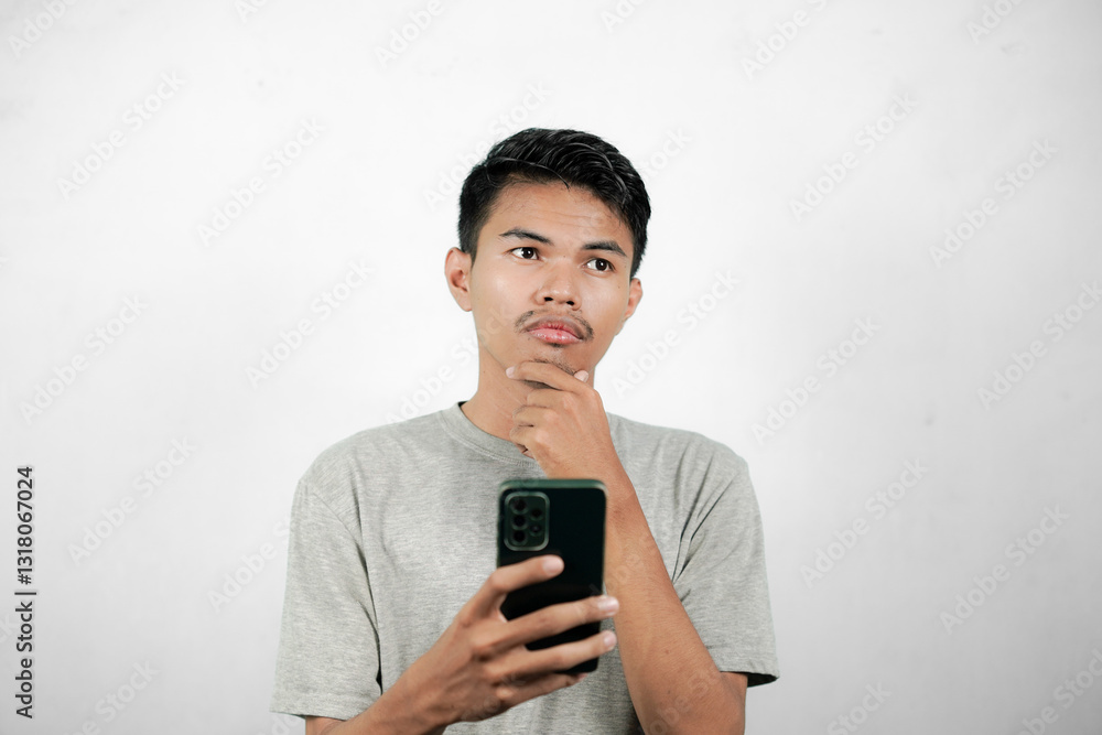 Portrait of asian man thinking while holding chin while looking at smartphone, young man isolated on white background Portrait of asian man thinking while holding chin while looking at smartphone, young man isolated on white background