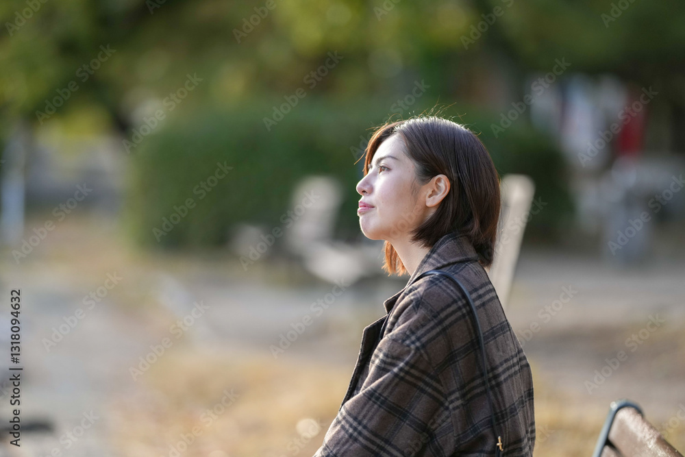 Winter at Ohori Park in Chuo Ward, Fukuoka City, Japan. A 29-year-old Japanese woman wearing a checkered coat. She is sitting on a bench along the pond. Winter at Ohori Park in Chuo Ward, Fukuoka City, Japan. A 29-year-old Japanese woman wearing a checkered coat. She is sitting on a bench along the pond.