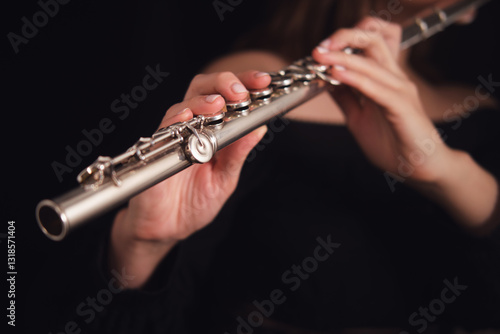 Musician's hands holding and playing a silver flute on a dark background. Studio music photography. Classical performance and wind instrument concept.
