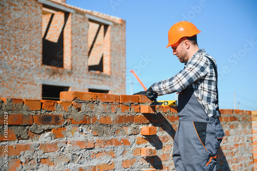 Male construction worker in uniform and helmet on construction of red brick house photo