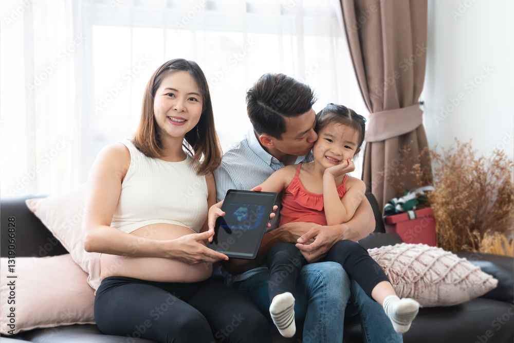 Asian pregnant mother with caring father and little daughter sitting on sofa at home, smiling and looking camera, holding tablet with ultrasound image of baby. Family, bonding and expectant parents Asian pregnant mother with caring father and little daughter sitting on sofa at home, smiling and looking camera, holding tablet with ultrasound image of baby. Family, bonding and expectant parents