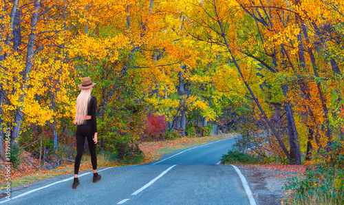 Obraz na płótnie A young woman walks on an asphalt road, autumn trees on either side of the road w salonie